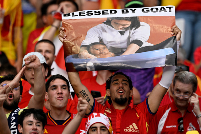 Pendukung Spanyol memegang poster Lionel Messi beropse dengan Lamine Yamal saat mengunjungi ruang ganti Barcelona sebagai bagian dari pemotretan kalender amal pada tahun 2007 menjelang pertandingan final UEFA Euro 2024 di Berlim, pada 14 Juli 2024. Foto: Ina Fassbender/AFP