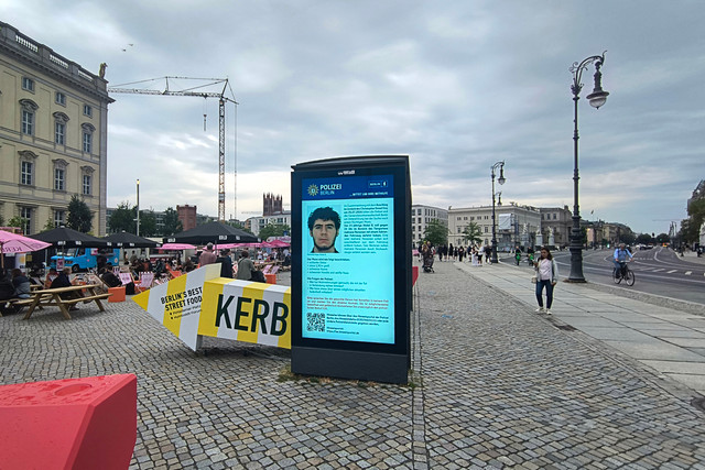 Papan pengumuman di halte bus pusat Kota Berlin menampilkan foto tersangka Abdul B., yang masih diburu polisi terkait serangan tabrak mobil saat parade Christopher Street Day (CSD), Minggu (26/7/2026). Foto: AFP