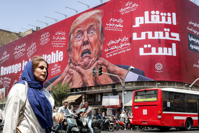 Seorang wanita berjalan melewati papan reklame besar yang menjanjikan pembalasan terhadap Presiden AS Donald Trump di sepanjang Jalan Jomhouri di pusat Teheran, Iran, Senin (27/7/2026). Foto: AFP