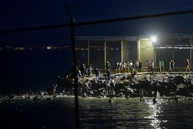 Para migran dari Maroko menyeberang ke Ceuta melalui laut dan berkumpul di dekat pagar perbatasan antara wilayah kantong Spanyol Ceuta dan Maroko, seperti yang terlihat dari Ceuta, Spanyol, Kamis (30/7/2026). Foto: Fabian Bimmer/REUTERS