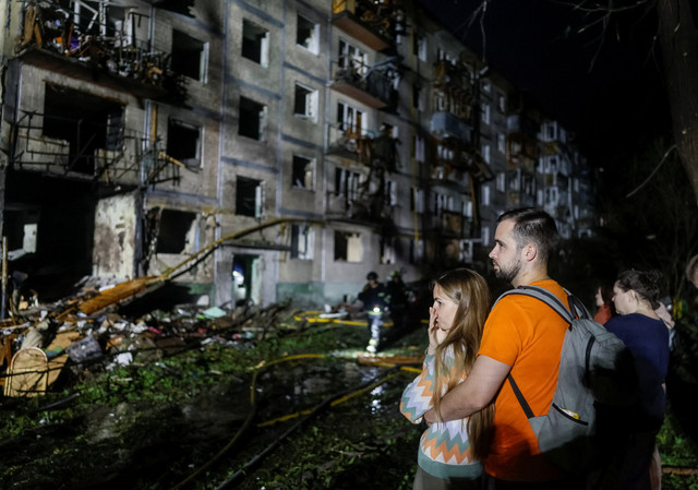 Warga berdiri di lokasi gedung apartemen yang terkena serangan rudal Rusia, di tengah serangan Rusia terhadap Ukraina, di Kiev, Ukraina, Sabtu (1/8/2026). Foto: Gleb Garanich/REUTERS