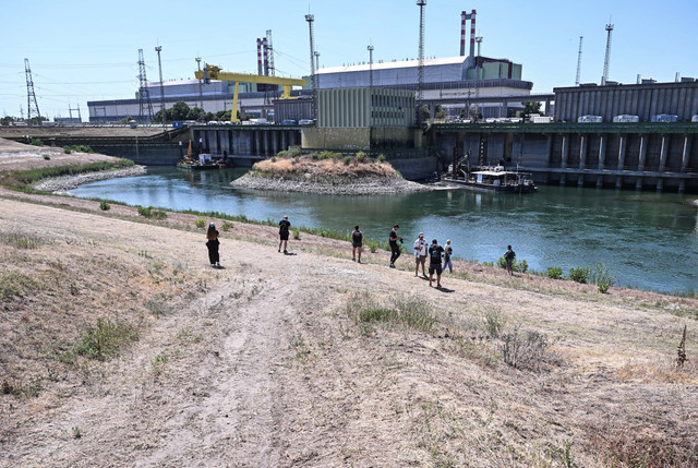 Para jurnalis berdiri di depan struktur pengambilan air dan kanal air dingin Pembangkit Listrik Tenaga Nuklir Paks yang menggunakan air dari Sungai Danube di Paks, Hungaria, Jumat (31/7/2026). Foto: ATTILA KISBENEDEK/AFP