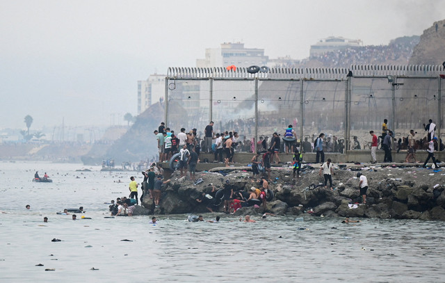 Migran dari Maroko berkumpul di dekat pagar perbatasan saat melintasi perbatasan Spanyol, berenang melintasi laut, terlihat dari Ceuta, Spanyol, Jumat (31/7/2026). Foto: Fabian Bimmer/REUTERS