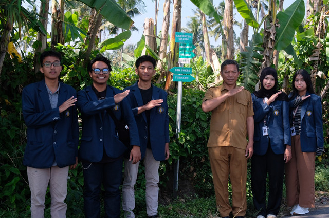 Foto mahasiswa KKN FSTeM UB bersama Kepala Desa Sukoanyar di depan plang Jejak Sukoanyar.