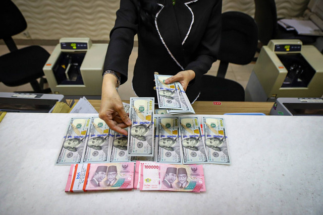 Seorang petugas menunjukkan pecahan dolar AS dan Rupiah di salah satu tempat penukaran mata uang asing di Kwitang, Jakarta, Senin (9/12/2024). Foto: Iqbal Firdaus/kumparan