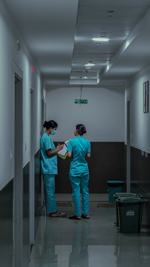 Dua tenaga kesehatan berdiskusi mencatat data di lorong rumah sakit. Foto: pexels.com/Adarsh Mp