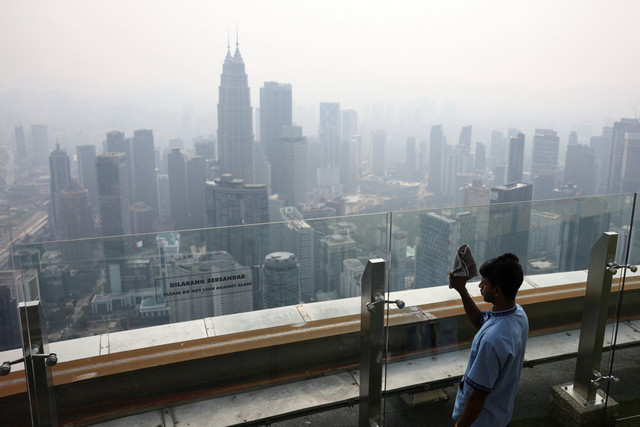 Seorang petugas kebersihan menyeka dinding kaca yang menghadap cakrawala pusat kota yang diselimuti kabut asap di Kuala Lumpur, Malaysia, Rabu (12/8/2026). Foto: Hasnoor Hussain/REUTERS