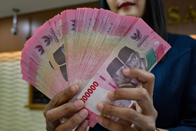 Petugas penukaran uang menunjukkan uang Rupiah di sebuah gerai penukaran mata uang di Jakarta (12/5/2026). Foto: Bay Ismoyo/AFP