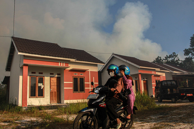 Warga melintas dengan latar belakang kepulan asap akibat kebakaran lahan di kawasan permukiman Tegal Sari, Palangka Raya, Kalimantan Tengah, Jumat, (7/8/2026). Foto: ANTARA FOTO/Auliya Rahman