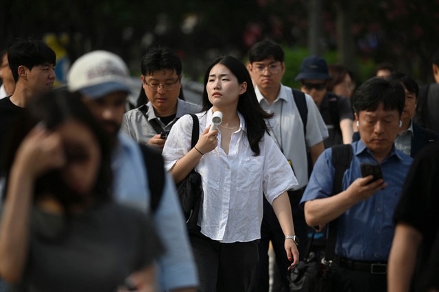 Seorang wanita mengibas kipas untuk mendinginkan diri saat menyeberang jalan di Seoul, Korea Selatan (28/7/2026). Foto: Greg Baker/AFP
