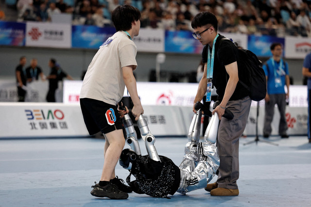 Para insinyur memindahkan robot humanoid setelah robot tersebut menyelesaikan kontes tari jalanan, selama Pertandingan Robot Humanoid Dunia 2026 di National Speed Skating Oval di Beijing, China, Selasa (25/8/2026). Foto: Tingshu Wang/REUTERS