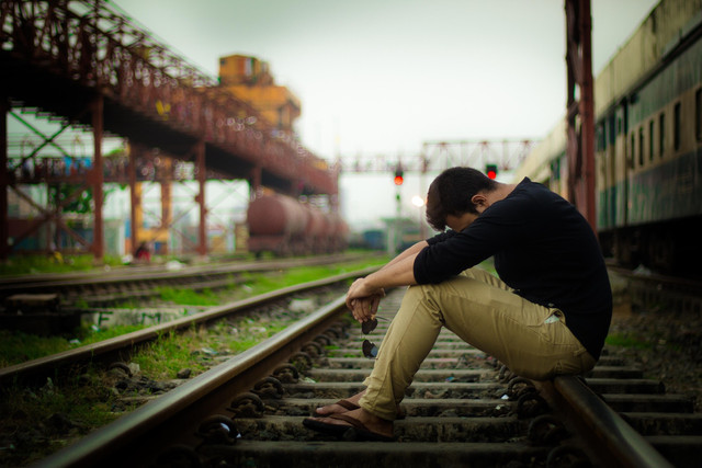 Seseorang duduk di atas rel kereta dengan kepala tertunduk, menciptakan suasana tenang dan penuh perenungan. Foto: Pixabay