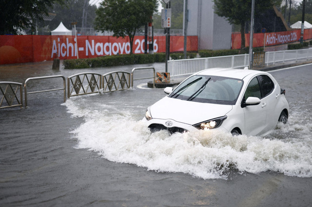 Sebuah mobil melaju di jalan yang tergenang air akibat hujan deras sementara spanduk untuk Asian Games Aichi-Nagoya terlihat di latar belakang di Nagoya, Jepang tengah, Selasa (8/9/2026). Foto: Kyodo/via REUTERS