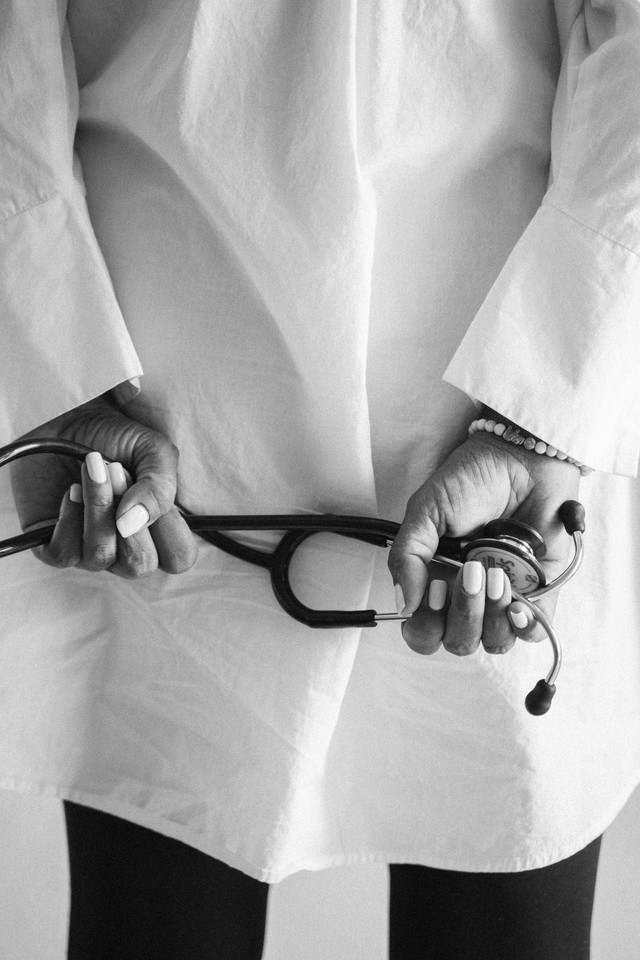 Black and white image of a doctor holding a stethoscope behind their back (by Anna Arazevich)(https://www.pexels.com/photo/woman-hands-holding-stethoscope-7904474/)
