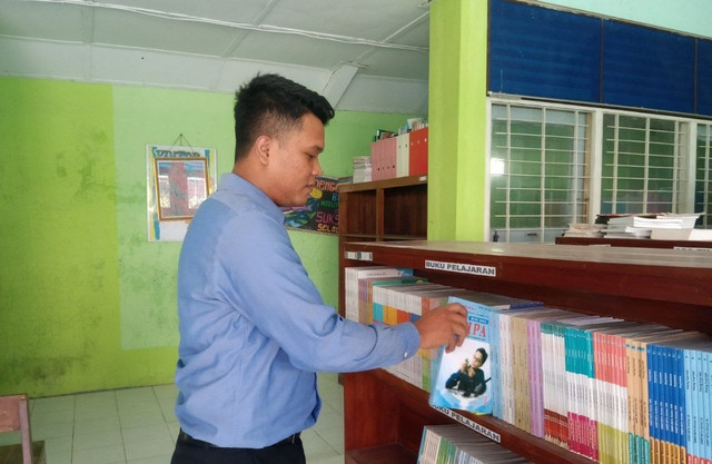 Pak Jalu (31) sebagai Kepala Perpustakaan SMP Negeri 2 Godean sedang memilih dan mengambil buku di rak perpustakaan. Foto: Kristiani Kundimang. Selasa (15/09/2026)