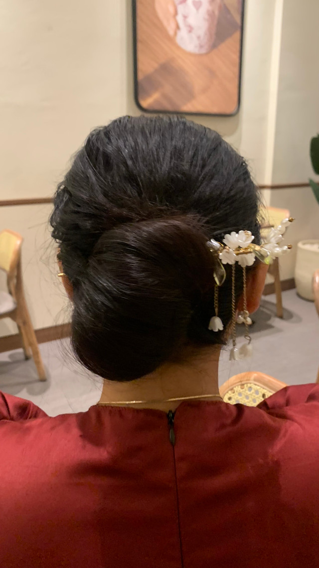 Perempuan dengan sanggul tradisional dan busana berwarna merah dalam sebuah aktivitas sehari-hari. Foto ini menggambarkan salah satu bentuk representasi perempuan dalam kehidupan sosial dan budaya.Sumber: Dokumentasi pribadi.