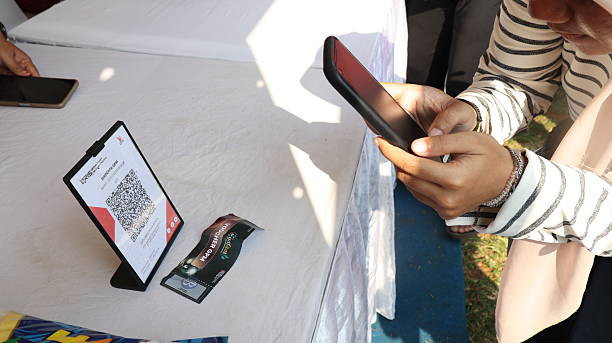 ilustrasi : Pelanggan menggunakan smartphone untuk memindai kode QRIS dan membayar belanjaan secara digital di warung pasar, menunjukkan kenyamanan pembayaran nontunai. Karya:Lutfi Hanafi/iStock