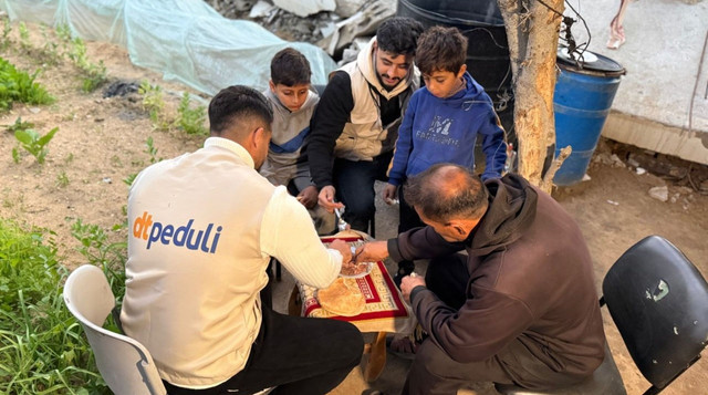 Warga Pengungsi di Gaza sedang makan bersama dengan relawan DT Peduli di sekitar pengungsian (Sumber: DT Peduli)