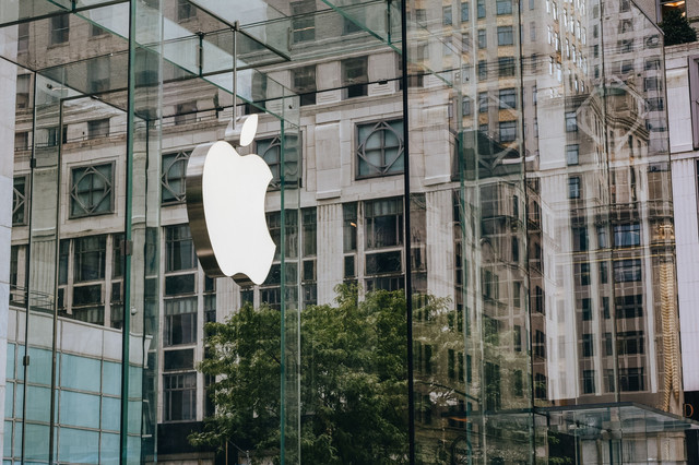 Logo Apple pada fasad kaca modern dengan refleksi perkotaan, menangkap arsitektur kontemporer. Foto: Pexels