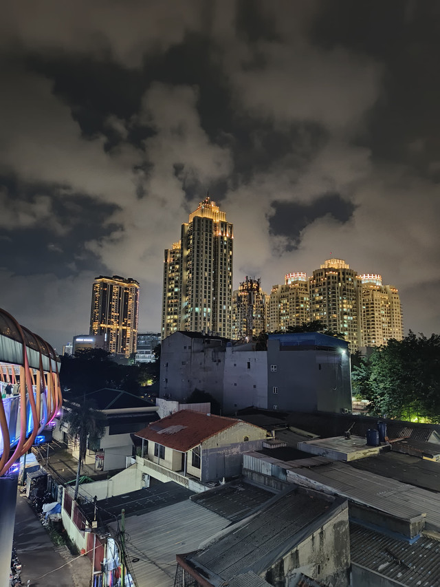 Kontras pemandangan gedung pencakar langit dan kawasan pemukiman warga di malam hari. Gambar ini merefleksikan dinamika kehidupan serta tantangan ekonomi yang dihadapi kelas menengah di perkotaan. (Foto: Dok. Pribadi)