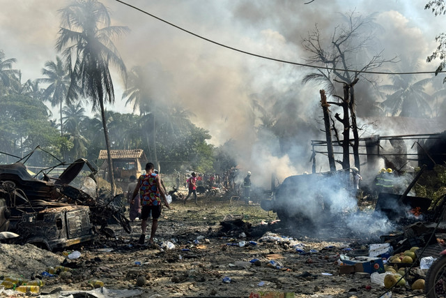Orang-orang berjalan melewati asap dan puing-puing yang masih berasap setelah serangan udara militer di sebuah pasar dan jembatan di dekatnya di Kyauktaw, negara bagian Rakhine Barat, Myanmar, Senin (28/9/2026). Foto: AFP