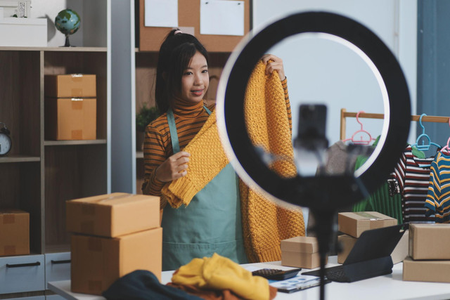 Pelaku UMKM sedang melakukan live shopping untuk mempromosikan produk pakaian dan menarik minat konsumen melalui siaran langsung. Foto : ShutterStock