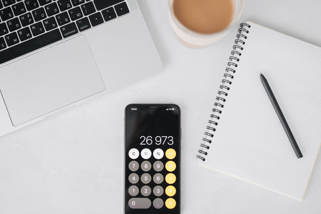 Ilustrasi aktivitas pencatatan keuangan usaha menggunakan laptop, ponsel, kalkulator, dan buku catatan sebagai gambaran pengelolaan omzet UMKM (foto: Polina Tankilevitch/ pexels)