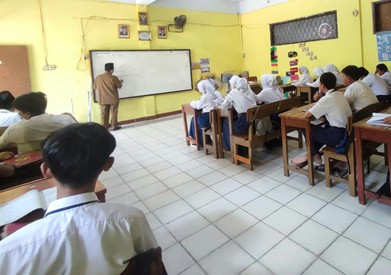 Suasana kegiatan belajar mengajar siswa SMP berseragam putih biru di kelas saat guru sedang menjelaskan materi di papan tulis. Sumber: Foto ini merupakan hasil pemotretan sendiri yang menampilkan suasana kegiatan belajar mengajar di dalam ruang kelas MTs. Avicenna (Foto: Dok. Pribadi).