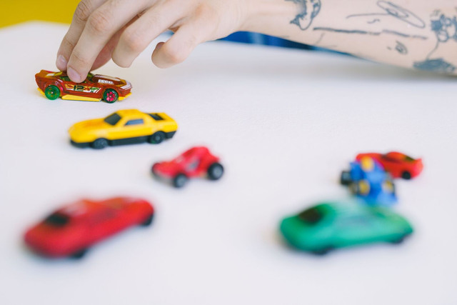 Ilustrasi orang dewasa sedang memainkan mobil-mobilan kecil di antara beberapa mobil mainan berwarna-warni. (Pexels/Shvets Production)