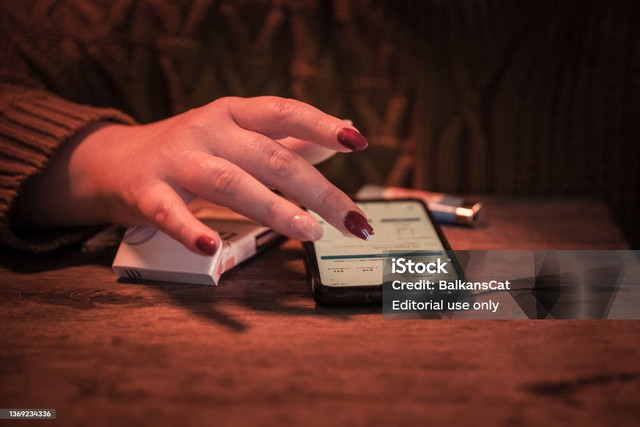 Seseorang sedang menggunakan ponsel di atas meja dengan tangan menyentuh layarnya. (Sumber : iStock)