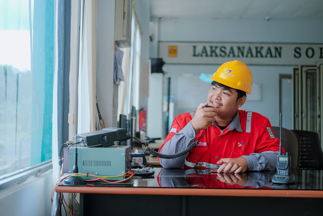 ilustrasi: Seorang petugas tampak menjalankan kewajibannya dengan mengenakan perlengkapan keselamatan dan menggunakan alat komunikasi untuk mendukung kelancaran aktivitas operasional. (sumber: Pexels/Mudrik Sulaiman)