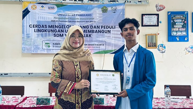 Ketua Tim Ecofinity Universitas Pamulang menyerahkan sertifikat kepada dosen pembimbing, Yhonanda Harsono, S.Si., M.M., dalam kegiatan PKM di SMK Bhakti Karya Sawangan pada 8 Oktober 2026. Dokumentasi pribadi.