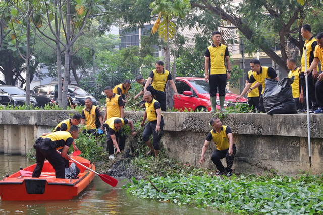 Personel Polres Metro Bekasi Kota melaksanakan aksi pembersihan eceng gondok di aliran Kali Baru, tepat di depan Markas Polres Metro Bekasi Kota, Jumat (16/10/2026). Foto: Dok. Istimewa