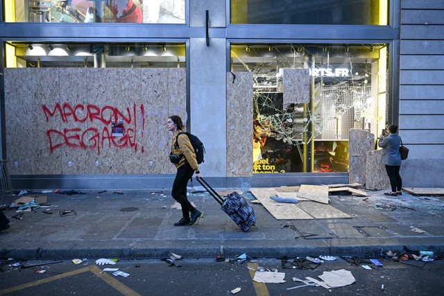 Seorang pejalan kaki melewati toko yang rusak sementara yang lain mengambil foto sehari setelah protes nasional menentang "tingginya biaya hidup", di Paris, Minggu (18/10/2026). Foto: MATTHIEU RONDEL/AFP