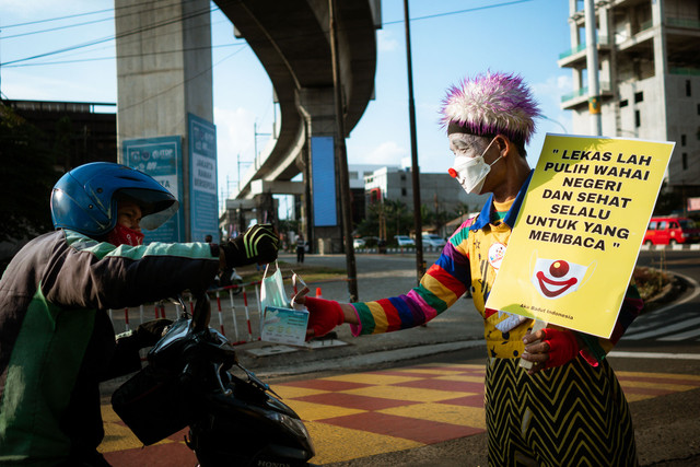 Anggota komunitas Aku Badut Indonesia (ABI) melakukan aksi kampanye protokol kesehatan COVID-19 dengan membagikan masker serta membawa poster di kawasan Fatmawati Jakarta, Senin (12/7/2021). Foto: Jamal Ramadhan/kumparan