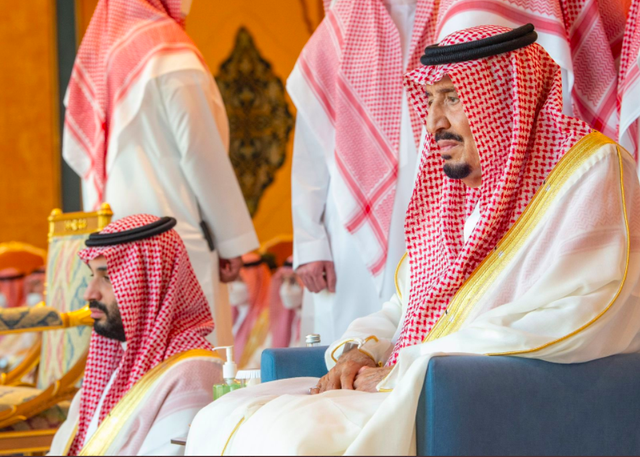  Pangeran MBSduduk di bawah di sebelah Raja Salman yang duduk di kursi dalam rangkaian salat Id di Masjidil Haram, Senin (1/5/2022). Foto: Makkah Region