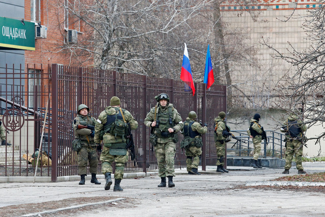 Militer Rusia mengibarkan bendera Rusia dan separatis yang memproklamirkan diri sebagai Republik Rakyat Luhansk (LNR) di luar cabang bank Oschad di Stanytsia Luhanska, Luhansk, Ukraina. Foto: Alexander Ermochenko/REUTERS