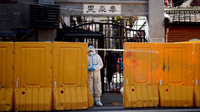 Seorang pekerja dengan pakaian pelindung berdiri di belakang penghalang yang menutup area perumahan di bawah lockdown di Shanghai, China, Rabu (30/3/2022). Foto: Aly Song/REUTERS