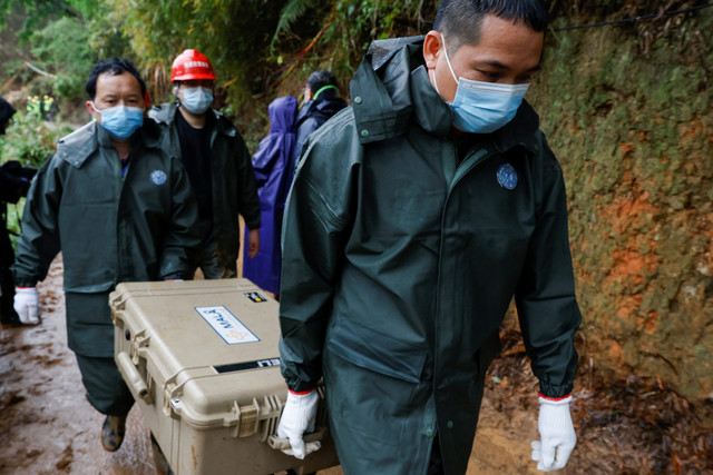 Pekerja membawa koper di lokasi jatuhnya pesawat China Eastern Airlines Boeing 737-800 di Wuzhou, Daerah Otonomi Guangxi Zhuang, China, pada Kamis (24/3/2022). Foto: Carlos Garcia Rawlins/Reuters
