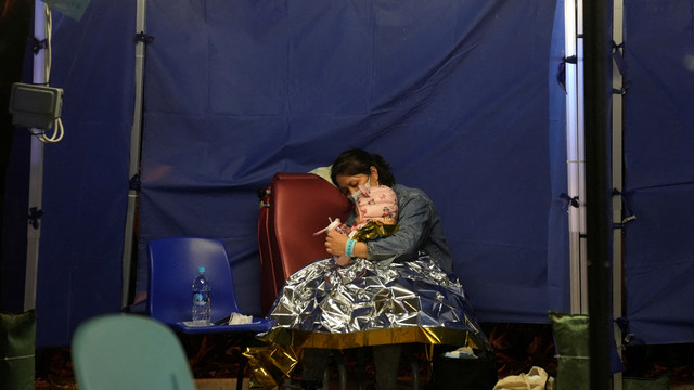 Pasien wanita bersama anaknya duduk di tempat tidur di area perawatan darurat di luar rumah sakit, di Hong Kong, China, Kamis (17/2/2022). Foto: Lam Yik/REUTERS
