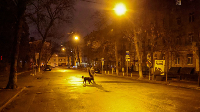 Seorang wanita berjalan di sepanjang jalan yang sepi dengan anjingnya beberapa jam sebelum jam malam di Kyiv, Ukraina, Kamis (24/2/2022). Foto: Umit Bektas/Reuters