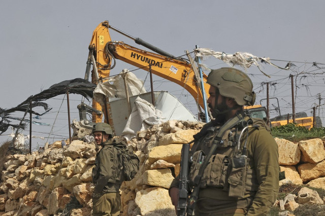 Seorang tentara Israel berjaga-jaga ketika alat berat menghancurkan rumah keluarga Palestina, di selatan kota Hebron, Tepi Barat pada Rabu (9/3/2022)
Foto: Hazem Bader/AFP