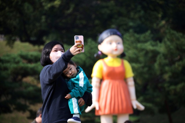 Warga swafoto dengan boneka raksasa dalam serial Squid Game yang dipamerkan di sebuah taman di Seoul, Korea Selatan. Foto: Kim Hong- Jihee/REUTERS