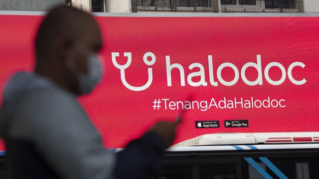 Warga mengoperasikan telepon pintarnya dengan berlatar belakang sebuah reklame produk startup nasional di Jalan Jenderal Sudirman. Foto: ANTARA FOTO/Aditya Pradana Putra