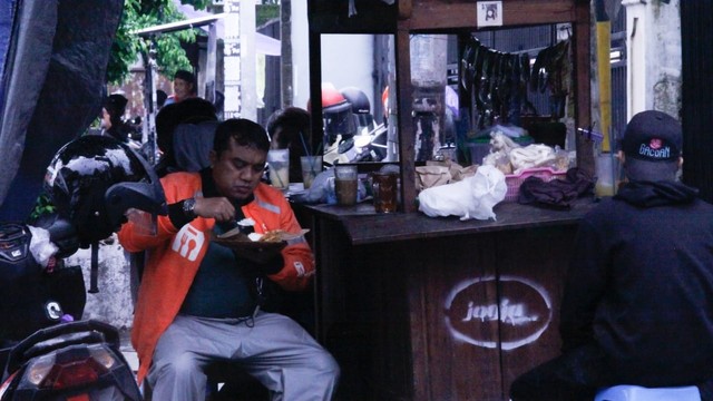Seorang pengemudi ojek online makan di sebuah angkringan di Yogyakarta. Foto: Widi Erha Pradana