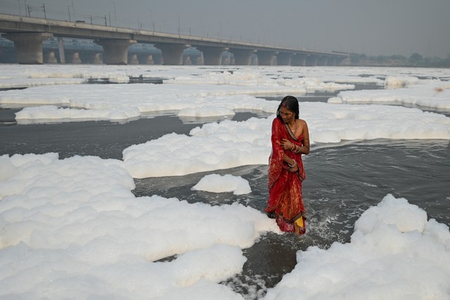 Seorang perempuan berdiri di perairan sungai Yamuna sebagai bagian dari ritual untuk festival Hindu Chhat puja di tengah busa yang diciptakan oleh polusi di air di New Delhi pada 8 November 2021. Foto: Sajjad Hussain/AFP