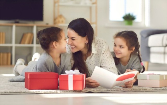 Keluarga lucu merayakan Hari Ibu di rumah. Wanita muda yang bahagia berbaring di lantai bersama anak-anaknya, membaca kartu ucapan, berterima kasih kepada anak-anak atas hadiahnya, menyentuh hidung dan orang Eskimo berciuman dengan putrinya. (Shutterstock.com/Studio Romantic)