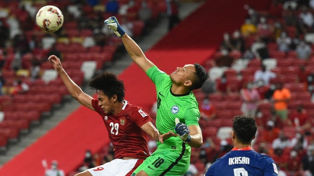 Pemain Singapura Hassan Sunny (tengah) mencoba untuk membersihkan bola di samping pemain Indonesia Hanis Saghara Putra (kiri) pada pertandingan leg kedua semifinal sepak bola Piala AFF Suzuki 2020. Foto: Roslan R/AFP