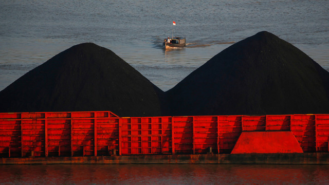 Seorang pria berdiri di atas kapal saat tongkang batubara mengantri untuk ditarik di sepanjang sungai Mahakam di Samarinda, provinsi Kalimantan Timur, Indonesia. Foto: REUTERS/Willy Kurniawan