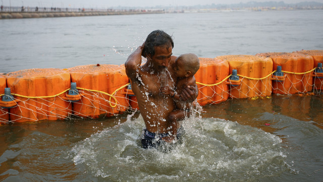 Seorang umat Hindu berenang saat menggendong putranya di Sangam, pertemuan sungai Gangga, Yamuna dan Saraswati selama festival Magh Mela, di Prayagraj, India, Jumat (14/1). Foto: Ritesh Shukla/REUTERS